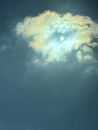 The image shows a sky with a large cloud formation. The sun is visible through the cloud, creating a bright, diffuse glow. The cloud itself is predominantly white with yellowish edges, suggesting sunlight filtering through its edges. The remaining sky is a muted blue-gray color, indicating overcast conditions. There is no identifiable information that would confirm the location is in Bnei Shimon Regional Council, Israel. There are no people, subjects, objects, actions, or interactions visible in the image beyond the cloud formation and sunlight.