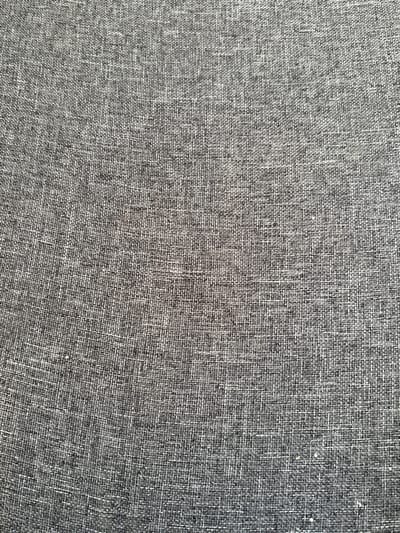 The image displays a close-up, overhead view of a textured grey fabric. The weave is clearly visible, showing interlacing threads that create a slightly rough, woven pattern. There are no people, animals, or discernible objects within the frame. The environment is a flat surface covered by this fabric. There is no information to connect this image to Koshkino, Russia.