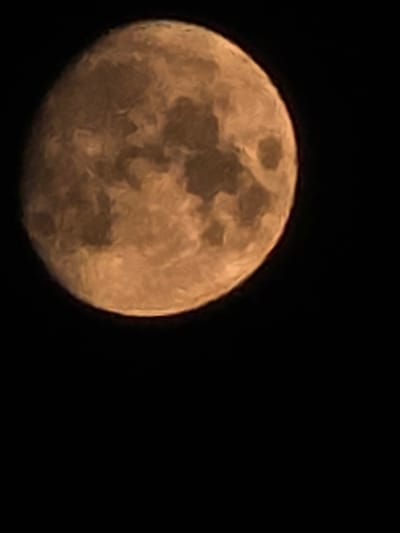 The image shows a close-up, slightly out-of-focus view of the moon against a dark night sky. The moon is a warm, orange-brown color with visible surface features, suggesting craters and maria. The composition is dominated by the moon, which occupies the upper left portion of the frame, with a large area of blackness to the right and below. There is no indication of the city of Montrouge, France, or any urban environment. The image is a straightforward astronomical photograph of the moon.