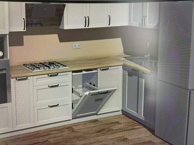 This is a digital rendering of a modern kitchen, not a photograph of a real location in Mirnoye, Ukraine. The kitchen features white cabinetry with dark handles, a light-colored countertop, and a stainless steel range hood. A gas cooktop is visible on the countertop. To the right, a stainless steel refrigerator is partially visible. In the foreground, a cabinet door is open, revealing a pull-out shelving unit. The floor is made of wood-look planks. There are no people or any indication of activity.