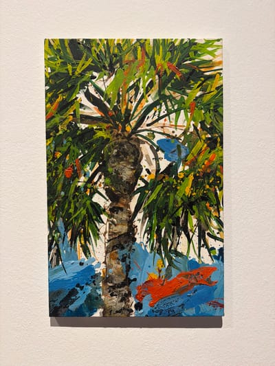 This is a medium shot, eye-level, horizontal photograph of an abstract acrylic painting mounted on a textured white wall. The painting depicts a close-up, impressionistic view of what appears to be pine needles and a branch. Dominant colors include various shades of green, brown, black, and blue, with accents of orange and yellow. The brushstrokes are dynamic and energetic, with visible splatters and thick applications of paint, suggesting a sense of movement and texture. The background is primarily white, with abstract splashes of blue, orange, and black paint on the right side of the canvas, creating a contrast with the natural elements on the left. The lighting suggests ambient, likely indoor lighting, casting a subtle shadow to the right of the painting. There is no discernible text or any indication of a specific time of day, weather, or explicit emotion within the artwork itself. The setting is a plain white wall, likely in a gallery or home environment. The subject matter appears to be a stylized representation of nature, possibly a pine tree branch, rendered in a bold, abstract style.