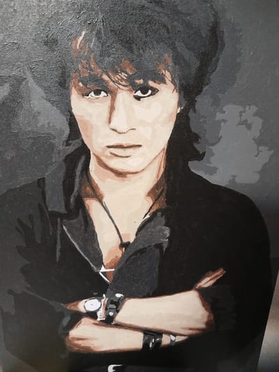 This is a painting of a young man with dark, messy hair and a serious expression. He is wearing a black collared shirt with the top few buttons undone, revealing a necklace with a pendant. He also wears a watch on his left wrist and multiple bracelets on both wrists. His arms are crossed in front of him. The background is dark and abstract, with varying shades of gray and hints of lighter gray cloud-like shapes. The painting style is somewhat impressionistic, with visible brushstrokes and a limited color palette focusing on dark tones, flesh tones, and browns. The lighting appears to be coming from the front, casting subtle shadows. The overall mood is somber and introspective. There is no visible text in the image.