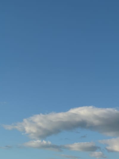 The image shows a clear blue sky with a few scattered clouds. The clouds are white and puffy, and they are located in the lower part of the image. The sky is a light blue color, and it is clear and cloudless in the upper part of the image. The image was taken on a sunny day. There are no people or objects visible in the image. The image depicts an outdoor scene.