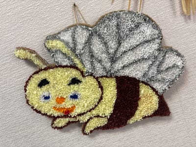 The image shows a handcrafted bee decoration made of crumpled paper. The bee has a yellow head with black eyes and blue and orange accents for its mouth. It has brown and yellow striped wings, and grey and yellow wings. The decoration is hanging on a textured white wall. The location in Ветрынскі сельскі Савет, Belarus, is not visible in the image.