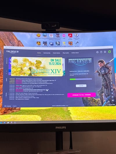 The image shows a computer screen displaying the Final Fantasy XIV launcher. The launcher is in the process of updating the game, with a progress bar indicating "Time Remaining: Approximately 38 minutes." The background of the launcher features artwork from the game, including characters and scenery. There is also a news feed on the left side of the screen detailing recent game updates and events. The computer itself is placed on a desk, with a webcam visible at the top of the screen. The overall environment appears to be a home or office setting. The image does not contain any information related to the city of Karviná, Czechia.
