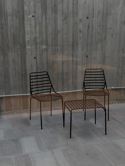 The image presents an interior scene featuring two chairs positioned against a concrete wall and a tiled floor. The wall is raw, grey concrete with horizontal markings. Two metal chairs are placed near the wall, one slightly ahead of the other. The chairs are composed of a metal frame and seat. The floor is covered with grey rectangular tiles. The image appears to be taken indoors with ambient lighting. The city of Chkalov, Armenia is not explicitly discernible from the visual information provided.