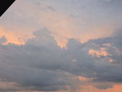 This is a media file of a sky with clouds. The subjects are the clouds themselves, which are dense and varied in texture. The scene is an outdoor setting, likely a landscape, with no specific objects or people visible.

The activity taking place is simply the natural phenomenon of clouds moving across the sky. There are no specific events or actions depicted.

Notable details include the time of day, which appears to be either sunrise or sunset, given the warm, peachy hues of the sky interspersed with the grey clouds. The weather seems to be a mix of cloudy and clear conditions, with pockets of sunlight breaking through the clouds. There are no explicit location cues visible in the image itself, other than the provided context of Širvintos, Lithuania. The overall emotion evoked by the image is one of natural beauty and tranquility, with a hint of the dramatic provided by the contrasting colors of the sky.

There is no visible text in the media file.