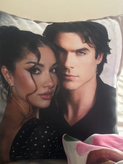 The image shows a rectangular throw pillow featuring a print of two people. The person on top appears to be a male with dark hair, light skin, and blue eyes, wearing a dark-colored shirt or jacket. The person below is a female with dark hair, light skin, and dark eyes, wearing a dark top with small white dots. The pillow is resting on a light-colored surface. The location of the image and the city of Mirkovo, Bulgaria cannot be determined based on the content of the image.