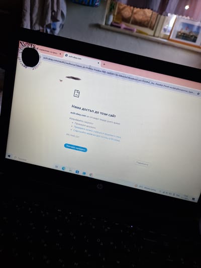 The image shows a laptop screen displaying an error message in Bulgarian, indicating that the website auth.ebay.com is not responding. The error message suggests checking the internet connection, firewall, and network diagnostics. The screen also shows a damaged area on the top left corner, which appears to be a physical defect on the screen. The laptop's keyboard and taskbar are partially visible. The surrounding environment is not discernible. There are no people or animals in the image. The location in the city of Raduvene, Bulgaria is not indicated in the image.