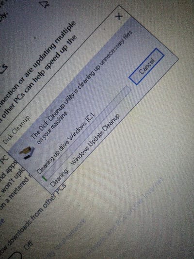 The image shows a laptop screen displaying a Disk Cleanup utility pop-up window in progress. The utility is "clearing up unnecessary files on your machine." The progress bar shows that "Cleaning up drive Windows (C:)" is completed, and "Cleaning Windows Update Cleanup" is in progress. The Cancel button is visible in the top right corner of the pop-up window. The laptop is located in Spokane, Washington, USA. The coordinates provided (latitude: 47.655, longitude: -117.379) correspond to a residential area in Spokane. The image captures a close-up of the laptop screen, focusing on the Disk Cleanup utility and its progress bar. The background shows a portion of the laptop screen, with blurred text. The image provides a glimpse into a user's computer activity and indicates that they are performing a Disk Cleanup task.