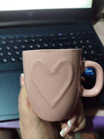 A pink mug with a heart embossed on its surface is held in someone's hand. The background shows a laptop keyboard. No information suggests this is in Yerzhovo, Moldova.