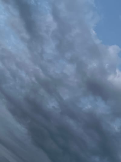 The image shows a close-up view of a turbulent sky filled with dark, wispy clouds. The clouds are predominantly gray with some hints of lighter shades, suggesting movement and depth. The texture of the clouds is rough and textured, with streaks and eddies formed by wind. A small patch of clear blue sky is visible in the upper right corner. The overall impression is one of an approaching storm or unsettled weather. The scene is devoid of any human presence or man-made objects.