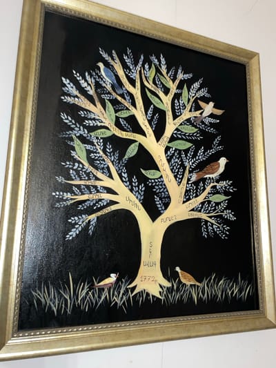The image shows a framed artwork, possibly a painting or print, depicting a stylized tree with branches bearing what appear to be names written in an Armenian script. The tree, predominantly rendered in a pale yellow color, contrasts against a solid black background. Leaves of varying shades of green and silver-blue are interspersed throughout the branches.

Several birds are positioned in and around the tree, suggesting a naturalistic, albeit stylized, setting. The lower right of the frame features what could be grass-like strokes, adding to the environmental context. The artwork is encased in a gold-toned frame.

The artwork has the inscription "1772," which is likely the year of the painting. The names on the tree are likely Armenian family names. There are no indications of the city of Aratashen, Armenia in the artwork.