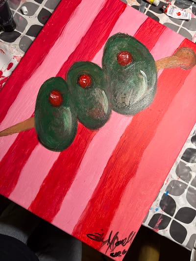 A painting depicts three olives on a skewer against a background of red and pink stripes. The olives are green with red pimentos inside. The background is alternating horizontal stripes of varying shades of red and pink. Tubes of paint are visible in the upper left and lower left corners of the image. A signature is in the upper right corner. The painting is on a surface covered in paint. The location is unknown, and there is no reference to Strömstad, Sweden, in the image.