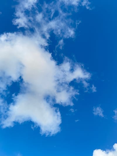 A bright blue sky with scattered white clouds. A sliver of the moon is visible in the upper left quadrant of the image, partially obscured by a cloud. The image appears to be taken from an outdoor perspective. There are no people, subjects, objects, actions, or interactions visible in the scene. The location is specified as Khang Tanjong, Indonesia.