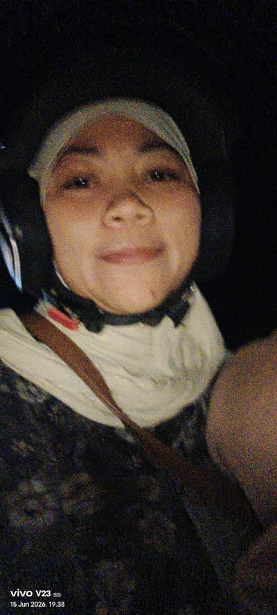 A medium shot selfie is captured in a dimly lit environment, likely at night, showing a young person wearing a light-colored hijab and a patterned garment. The individual is looking directly at the camera with a slight smile. A dark strap or belt is visible across their chest. The background is dark and appears to be outdoor or in a vehicle, with a timestamp at the bottom left indicating "15 Jun 2026, 19.38" and "vivo V23 5G". No specific landmarks or details are discernible to place the location within Rantopanjang, Indonesia.