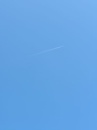 The image shows a clear blue sky with a faint contrail from an airplane. The contrail is a thin white line stretching diagonally across the upper right portion of the frame. There is no discernible urban environment, buildings, or people visible in the image. The location in Castiglione della Pescaia, Italy, is not identifiable from the visual content of the photograph.