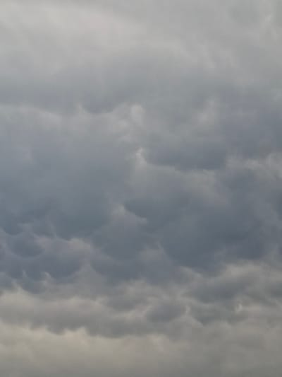 The image shows a close-up, eye-level, full-frame view of a cloudy sky. The clouds are a mix of grays and whites, with some appearing darker and more textured, suggesting they may be cumulonimbus or mammatus clouds. The lighting is diffused, consistent with an overcast day. There are no discernible landmarks or environmental features visible to indicate a specific location within Bulaev, Kazakhstan. The image does not contain any people, subjects, objects, or actions.