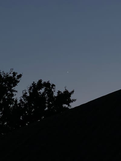 A small, bright celestial body, likely a planet or star, is visible in the dusky sky above Cairaclia, Moldova. Silhouetted trees and the dark outline of a roof occupy the lower portion of the frame, obscuring the ground and any potential human activity. The overall impression is of a quiet, late evening or early morning scene.
