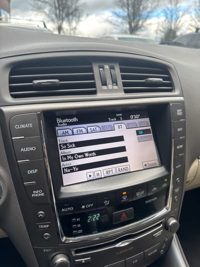 The image shows the dashboard of a Lexus, featuring the car's infotainment system displaying music from "In My Own Words" by Ne-Yo, specifically the song "So Sick". The system is connected via Bluetooth and is playing track 3, which is 30 seconds in. The climate control is visible, with buttons for temperature, auto, and defrost. A clock displays the time as 2:22. Additional buttons are labeled "Audio", "Disp", "Info Phone", and "PWR-VO".