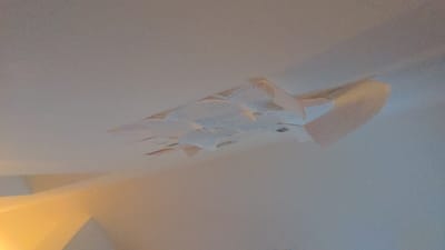 The image shows a white ceiling with several sheets of white paper stuck to it. The paper is arranged in a haphazard manner, with some sheets overlapping others. The sheets appear to be stuck to the ceiling with tape or glue. The image is taken from a low angle, looking up at the ceiling. The location is in Schwabach, Germany, with coordinates 49.333 latitude, 11.032 longitude. There are no people or other objects present in the image.