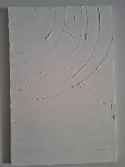 This is a photograph of a rectangular piece of abstract art, likely a painting or a textured wall hanging. The artwork is predominantly white or a very pale grey and features a textured surface.
The left side of the artwork displays a series of concentric curved lines, forming a fan or partial arc shape. These lines are created by raised ridges of material, suggesting a deliberate application technique.
The right side of the artwork is characterized by vertical lines and rectangular sections. Some of these sections have a rougher, almost pebbled texture, while others are smoother with visible brushstrokes or trowel marks. The overall impression is one of layered texture and subtle variations in surface finish.
There is no discernible activity or event taking place, as the image focuses solely on the artwork itself. The lighting is even, suggesting an indoor setting, and there are no clues about the time of day or weather. No people, specific objects, or location cues are visible within the artwork. There is no visible text. The context provided is Jerez, Spain, but this information cannot be verified from the image itself.
