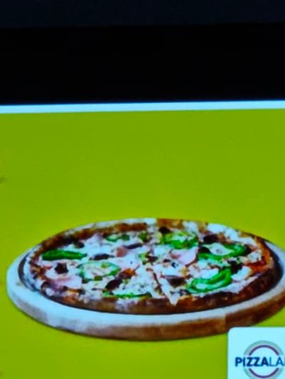 A pizza topped with green peppers and other ingredients is displayed on a wooden platter. The platter and pizza are positioned on a bright yellow surface. In the lower right corner, a logo featuring the word "PIZZALAB" is visible. The image appears to be taken from a screen or digital display. There is no evidence to indicate that the image is located in the city of Grohotno, Bulgaria.