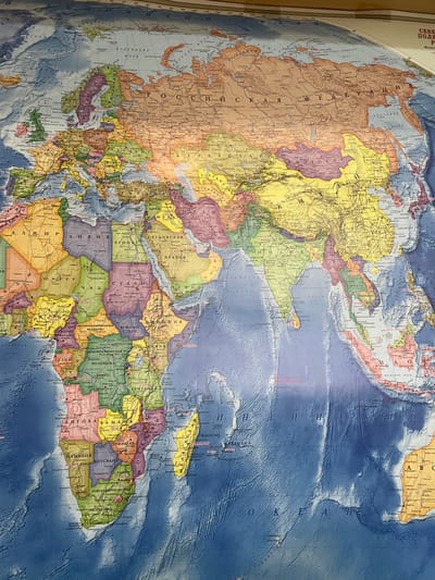 This media file presents a physical world map, primarily focusing on Eurasia and Africa, viewed from an elevated angle. The map is oriented approximately 90 degrees counter-clockwise from standard, with North pointing to the left and West towards the top.

The main subjects are the continents and oceans depicted on the map. Countries are distinguished by various colors such as yellow, green, purple, orange, and brown. Oceans are rendered in shades of blue, with darker tones indicating deeper waters and relief shading illustrating underwater topography. There is no activity taking place, as the image captures a static, physical map.

Notable details include the map's language, which is Russian (Cyrillic script). Prominently visible regions include the vast expanse of the "РОССИЙСКАЯ ФЕДЕРАЦИЯ" (Russian Federation) across the upper part of the image, the Indian Ocean ("ИНДИЙСКИЙ ОКЕАН") in the lower right, and a significant portion of Africa on the right side. Bodies of water like "БАРЕНЦЕВО МОРЕ" (Barents Sea), "ОХОТСКОЕ МОРЕ" (Sea of Okhotsk), and "КИТАЙСКОЕ МОРЕ" (Chinese Sea) are also labeled. Countries like "ЕГИПЕТ" (Egypt), "СУДАН" (Sudan), "ЮЖНЫЙ СУДАН" (South Sudan), "ЭФИОПИЯ" (Ethiopia), "САУДОВСКАЯ АРАВИЯ" (Saudi Arabia), "ИНДИЯ" (India), and "МАДАГАСКАР" (Madagascar) are clearly identifiable through their Cyrillic labels. The map shows minor wrinkles and folds, suggesting it's a physical, possibly laminated, wall map. "СЕВЕРНОЕ ПОЛЯРНОЕ" (Arctic Polar) is partially visible at the very top left, hinting at the full label for the Arctic Ocean. "Масштаб" (Scale) and "ABC" (likely an index or legend reference) are also visible.