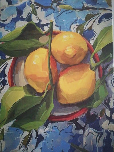 This is a painting of three lemons with green leaves, arranged in a shallow red-rimmed bowl, set against a blue and white floral patterned cloth. The lemons are bright yellow with highlights suggesting light reflection. The leaves are a deep green. The bowl's rim is a bold red. The background cloth is rendered with loose brushstrokes, creating an impressionistic effect of blue and white floral shapes. There is no indication of the city of Silifke, Turkey, in this image.