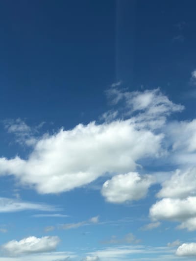 The image depicts a daytime sky in Rotherham, United Kingdom. The sky is predominantly blue with varying shades, ranging from a deep, saturated blue on the left side of the image to a lighter, more pale blue on the right. Scattered white clouds are present, with some appearing dense and fluffy while others are wispy and elongated. The image is rotated 90 degrees clockwise.