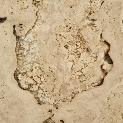 This is a close-up, abstract image of a textured surface. The dominant subject is the texture itself, which appears to be natural stone, possibly travertine or limestone, given its porous and somewhat irregular appearance. The color palette is earthy and muted, primarily shades of beige, cream, and light brown, with some darker, shadow-like areas adding depth.
The surface is characterized by a rough, matte finish with numerous small pits and cavities. A prominent feature is a larger, irregular opening or void in the stone, revealing a more granular, crystalline interior. This interior area is lighter in color and has a more broken, clumpy texture compared to the smoother outer surface. The edges of the opening are uneven and organic, suggesting natural erosion or formation.
There are no people, objects, or any discernible scene or setting. The image focuses solely on the textural details of the material. There is no indication of time of day, weather, or specific location cues beyond the provided context of Jerez, Spain, which might suggest a natural geological formation or a construction material used in that region. No text is visible in the image. The overall impression is one of natural beauty, texture, and the passage of time, emphasizing the inherent qualities of the stone.