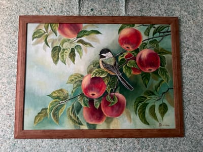 This is a framed oil painting of a bird perched on an apple tree branch. The bird, a chickadee, is positioned in the center of the image, facing left. It has black and white markings on its head and chest, with green and brown feathers on its back and wings. The branch is laden with several ripe, red apples and lush green leaves. The background is a soft, out-of-focus wash of pale green and yellow, suggesting a hazy, sunlit atmosphere. The painting is framed in a simple, dark wood frame. The artist's signature and the date "01.2016r." are visible in the lower right corner of the painting. The painting is displayed on a wall with a textured, speckled surface, which appears to be a light blue-green color. There is no indication of a specific city or location, including Osentsy, Russia, within the visual information provided by the image itself.
