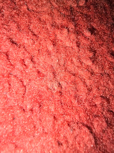 The image is a close-up, top-down view of a red fibrous material. The texture is dense and appears to be made of numerous fine, intertwined strands. The lighting creates highlights and shadows, emphasizing the three-dimensional nature of the material. There are no discernible objects, people, or actions. The location in Kostelec na Hané, Czechia is not visually represented in this image.