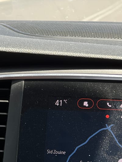 The image shows a close-up of a car's dashboard display, presenting a navigation map. The display indicates a location in "Sid Zouine", presumably near Saâda, Morocco, given that the city is listed next to the location. The temperature displayed is 41 degrees Celsius. The display also shows icons for phone and message functionalities. Adjacent to the screen is part of the car's interior, appearing to be a speaker grille.