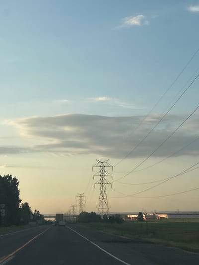 The image depicts a road leading into the distance with several power line towers forming a line along the right side of the road. The sky is a clear blue with a few wispy clouds. In the distance, there are some low buildings. The overall impression is that of a rural or semi-rural landscape. No specific details about the city of Ягуново, Russia, can be identified from the image alone.