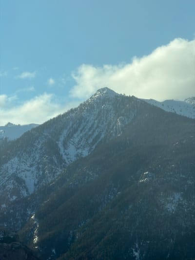The image shows a mountainside in Saint-Chaffrey, France. The mountain is covered in trees and snow. The sky is blue with some clouds.