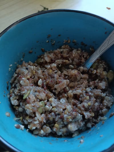 A close-up, overhead view captures a vibrant blue bowl filled with a mixture of grains and seeds, likely a porridge or healthy cereal. A silver spoon rests partially submerged in the food, ready for consumption. The background reveals a light-colored wooden surface, hinting at a dining table. This scene, a simple yet appealing depiction of food, is situated within the city limits of Miasskoye, Russia.