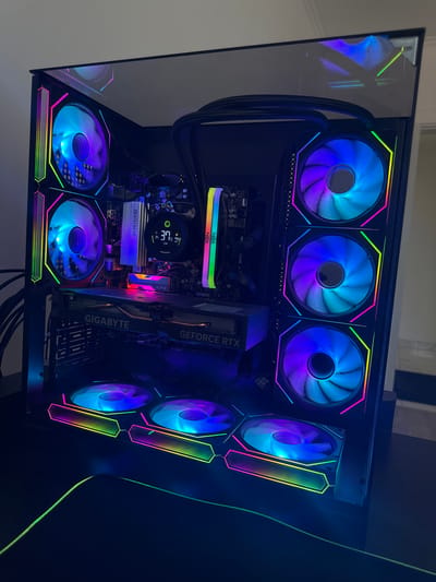 This media file shows the inside of a custom-built gaming computer, illuminated by RGB lighting from its fans and internal components. The computer is built inside a black case with a clear side panel, revealing a complex arrangement of hardware.

Prominently featured are multiple large, circular fans with vibrant RGB lighting that cycles through various colors, including blue, purple, and green. These fans are positioned at the top, front, and bottom of the case. A prominent graphics card, labeled "GIGABYTE GEFORCE RTX," is installed horizontally. Above the graphics card, a CPU cooler with a circular display showing temperature readings (currently 39°) is visible. Other components include RAM modules, likely labeled "NOX," and a motherboard.

The overall scene is one of a high-performance computer, likely used for gaming or demanding computational tasks. The dark interior of the case, contrasted with the bright, multicolored lights, creates a visually striking effect. There are no people or specific location cues to suggest the time of day, weather, or emotions. The only visible text includes brand names on components like "GIGABYTE," "GEFORCE RTX," and "NOX." The context of Vyzhnytsia, Ukraine, does not provide any visual information relevant to the image content itself.