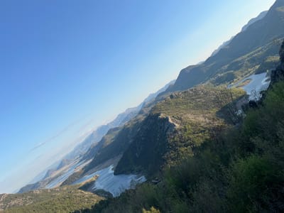 The image depicts a mountainous landscape with a clear blue sky. The mountains are covered with green vegetation and some rocky outcrops. There are long, narrow bodies of water nestled in the valleys between the mountains. The photograph appears to be taken from an elevated position, looking down at the landscape at an oblique angle. Based on the location, it is most likely to be the mountain near Rvaši, Montenegro. No people or animals are visible. The lighting suggests it is daytime.