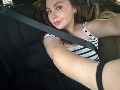 A woman is sitting in a car, wearing a black-and-white striped top and a seatbelt. She has brown hair and is looking at the camera. The car seats are black. The location is San Juan Tejupa, Mexico.