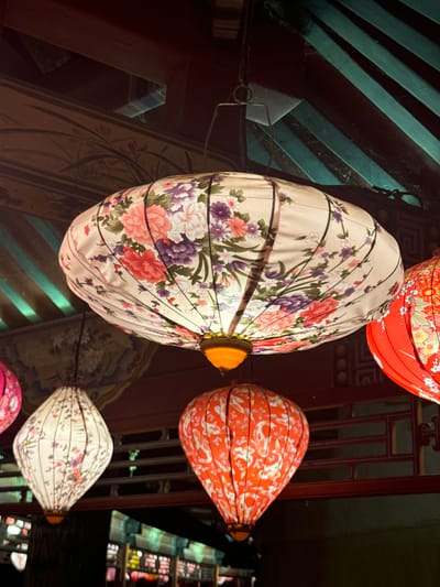 Several Chinese-style lanterns are suspended from the ceiling. The lanterns have different colors and floral patterns. The background shows architectural details. The location is Miyun District, China.