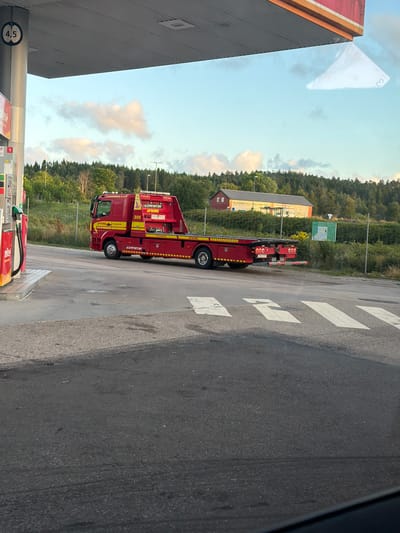 A red and yellow tow truck with "VIKING" branding is parked at a gas station. The truck has the number "305" on its side and a license plate reading "DEA 53Y". A gas pump is visible to the left of the truck. In the background, there is a building with text that reads "VÄLKOMMEN TILL STORA COOP TORP". The scene is set in Hogstorp, Sweden.