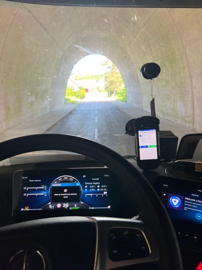 The image shows a view from inside a vehicle, likely a truck, driving through a tunnel. The dashboard instruments, including a speedometer, tachograph, and a navigation device, are visible. The speedometer indicates a speed of 39 km/h. The navigation device displays a route with a "ZEBRA" designation and a "NÄCHSTER STOPP" (next stop) scheduled between 12:30 and 15:00. The radio display shows "PRESLAVA x GALI" and indicates a song or radio station is playing. The outside environment is visible through the windshield as the vehicle exits the tunnel into daylight. The city is Dielheim, Germany.