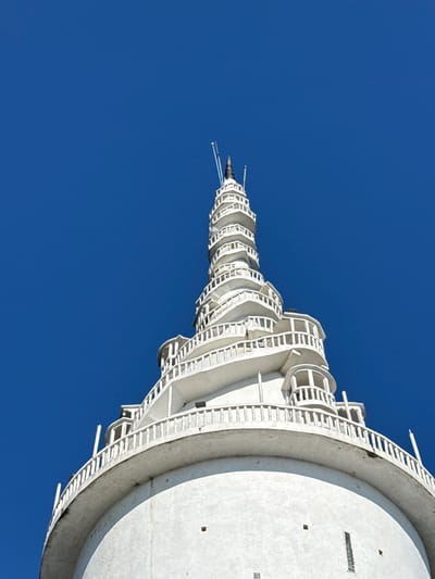 An upward perspective showcases a stark white, spiraling tower against a clear, deep blue sky. The structure's design features repetitive circular levels decreasing in size towards the top, resembling a futuristic antenna. A cylindrical base anchors the tower, exhibiting a smooth, concrete texture. The framework appears meticulously constructed with geometric precision, evoking a sense of modern architectural marvel.