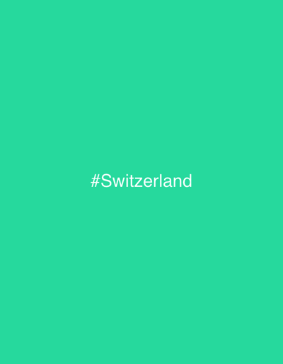The image displays a uniform, solid teal-colored background. Centered both horizontally and vertically on this background is the white text "#Switzerland" rendered in a sans-serif typeface. No other elements, such as people, objects, actions, or environmental details like landscapes, buildings, or natural features, are present. The image is a graphic representation devoid of a physical scene. The visual content does not provide any information to identify a specific location in Goldau, Switzerland, or any other geographical area.