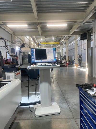 This image depicts an interior view of a modern industrial workshop or manufacturing facility in Podkletnoe, Russia. The setting is characterized by a high ceiling with exposed metal beams and industrial lighting fixtures, and a polished concrete floor. Various pieces of machinery and equipment are visible, suggesting a focus on precision manufacturing or engineering.
Prominently featured is a large computer monitor displaying technical data, graphs, and a circular diagram, likely indicating a control interface for a machine or a process monitoring system. Adjacent to the monitor is a white console or control unit. Other visible objects include what appears to be a blue tool chest with multiple drawers, various cables and electrical conduits, and other unidentifiable industrial equipment. There are no people visible in the frame.
The lighting suggests it is daytime, with natural light filtering in from windows or overhead structures, casting long shadows on the floor. The overall impression is one of an organized, functional, and technologically advanced workspace. No specific activity or event is clearly depicted, but the presence of machinery and monitoring systems implies ongoing operations. No readable text is discernible on the machines or equipment.