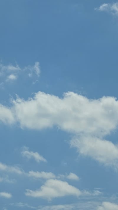 The image is a vertical, eye-level, medium shot of a blue sky with scattered white clouds. The clouds are primarily cumulus and cirrus formations, with some appearing thin and wispy while others are more dense and fluffy. The sky is a clear, light blue, suggesting a daytime scene. There are no visible structures, people, or any other objects within the frame. The location in Calau, Germany is not discernible from the image content itself.