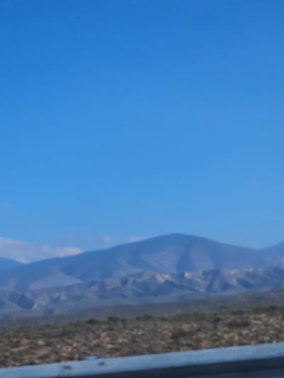 A partly clear, bright blue sky fills much of the left frame. Along the right side, a semi-transparent, crumpled material partially obscures a patch of brown and green vegetation. A gray, metallic-looking edge is visible at the far right border. The image is taken at an angle, presenting a distorted or tilted view of the objects.