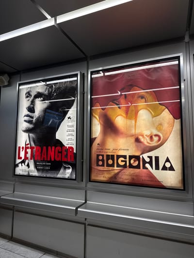 Two movie posters are displayed vertically. The top poster features a stylized image of a bald head, with geometric shapes and the word "BUGONIA" in bold letters. It lists Emma Stone and Jesse Plemons. The bottom poster showcases a black-and-white image of a man's face with "L'ETRANGER" prominently displayed. Text below credits François Ozon and Albert Camus, also listing actors Benjamin Voisin, Pierre Lottin, and Denis Lavant.