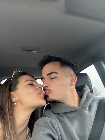 A photograph depicts two individuals, a male and a female, kissing in what appears to be the interior of a car. The interior is gray. The male is wearing a gray hooded sweatshirt. The image is oriented in a portrait format but appears to be rotated clockwise, suggesting the subjects are reclined. The location, Cherna Gora, Bulgaria, is not discernible from the visual information available.